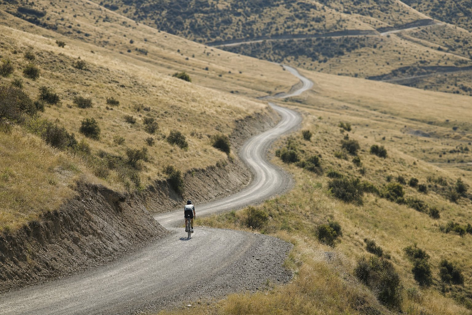 A lone cyclist on a winding gravel road cutting through rolling hills