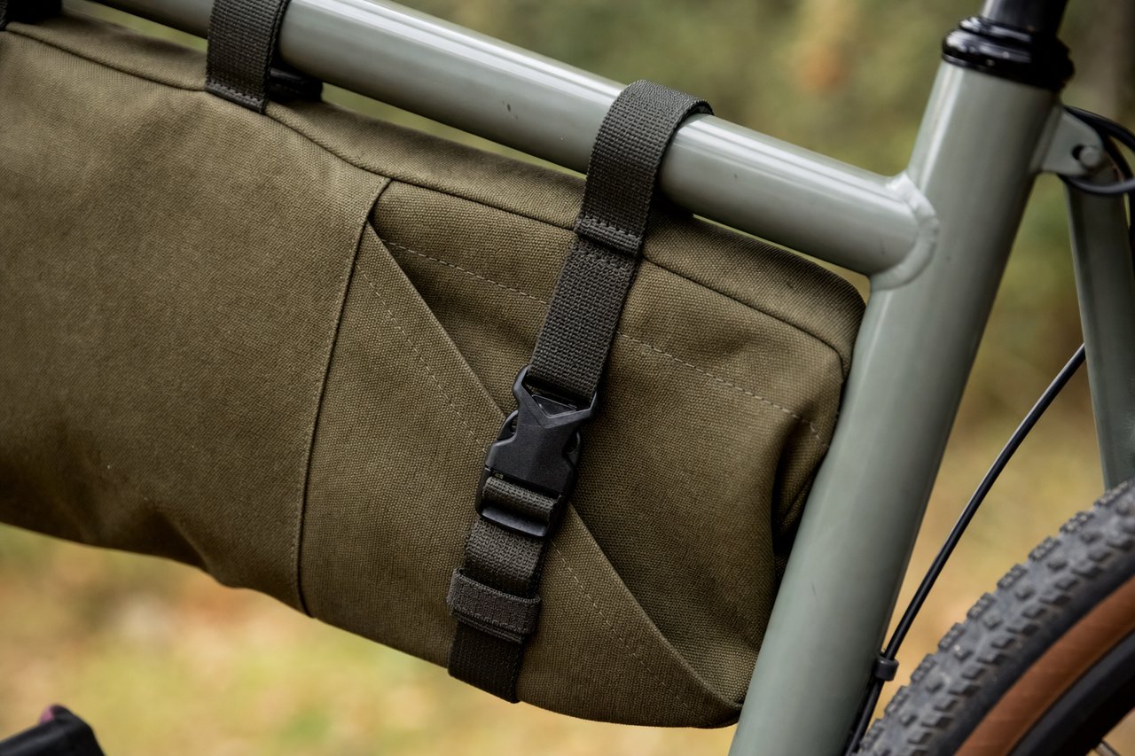 Close-up of a canvas frame bag's buckle and strap detail mounted on a bike's top tube
