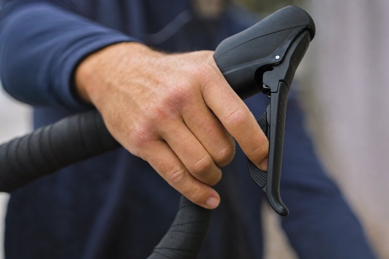 A hand squeezing a bicycle brake lever on the handlebar, checking lever travel and feel