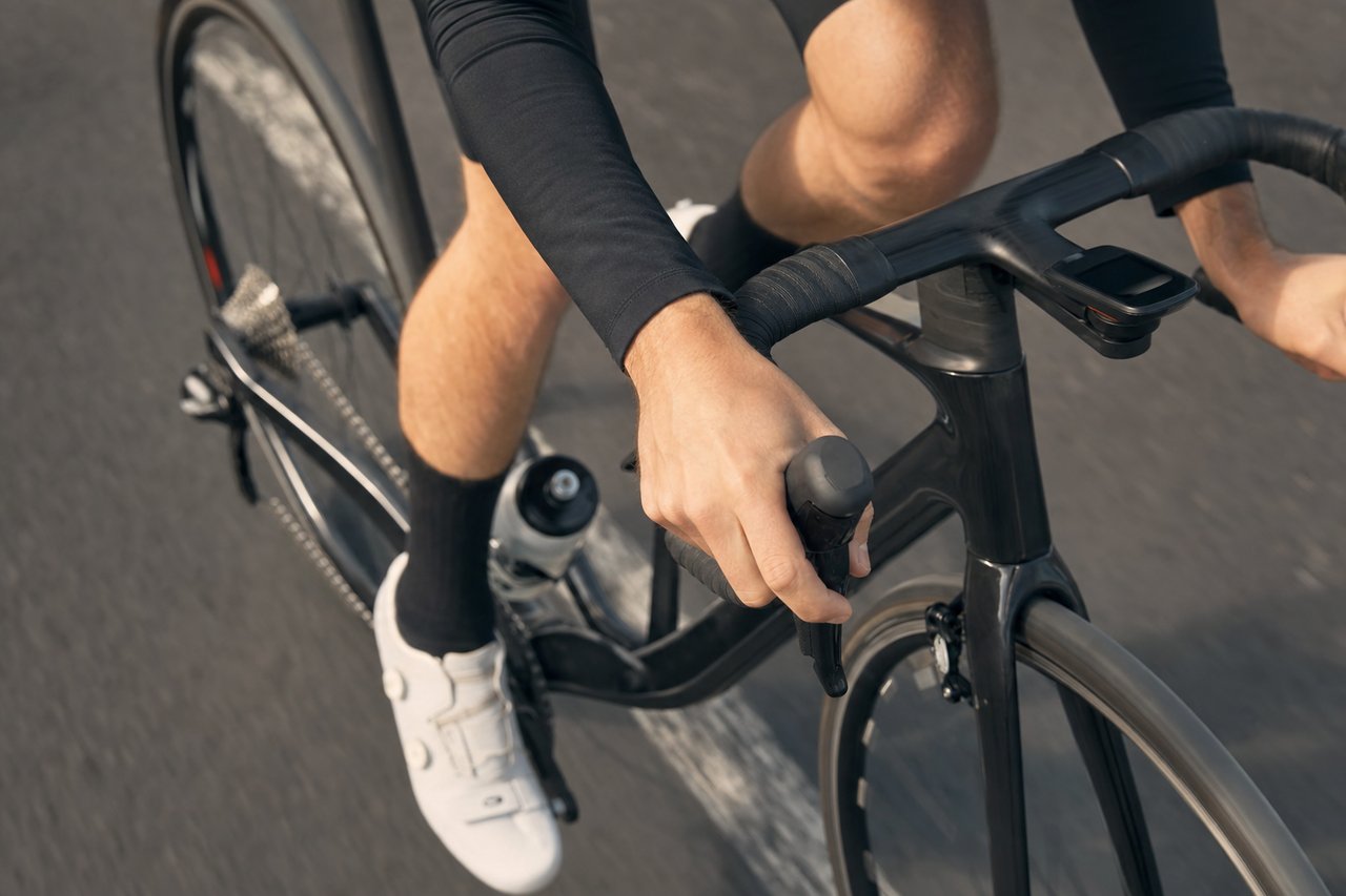 Close-up of a cyclist's hand operating a shift lever on a drop-bar road bike while riding
