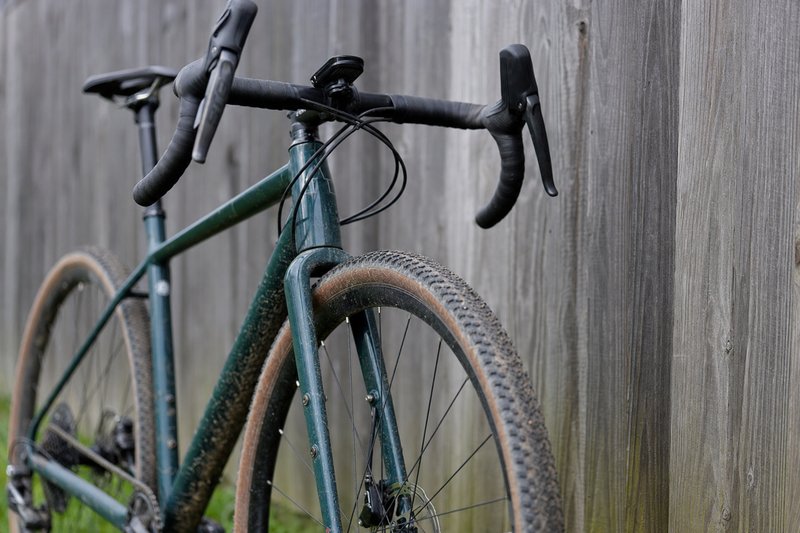 A three-quarter close-up of a gravel bike's front end showing drop bars, a wide knobby tire and generous fork clearance