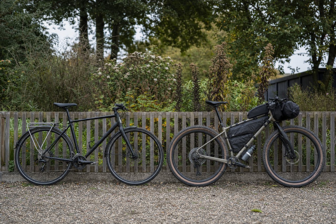 An everyday flat-bar hybrid bike parked beside a fully loaded dedicated bikepacking bike against a wooden fence