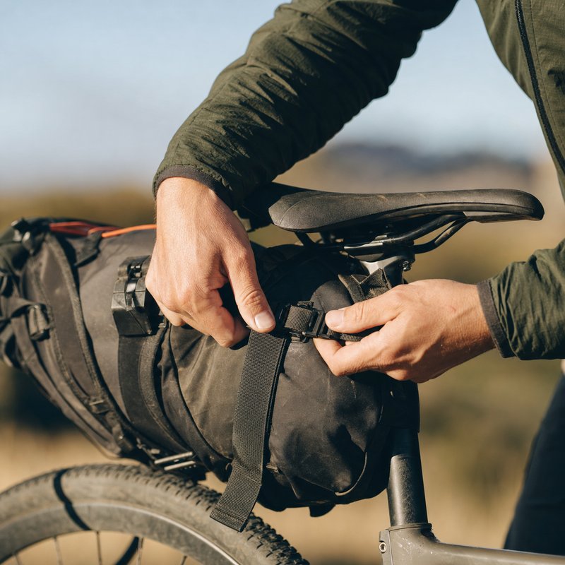Close-up of hands buckling a strap on a bikepacking seat pack
