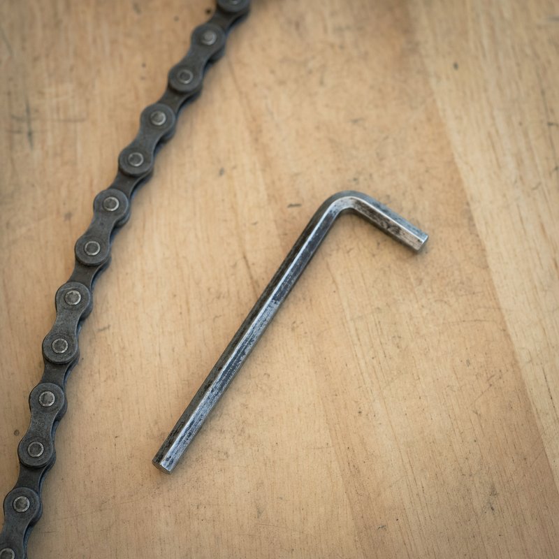 A single Allen key resting on a workbench beside a bicycle chain
