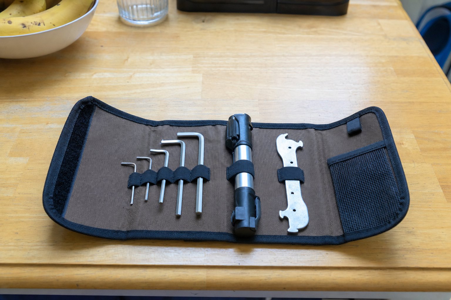 A compact canvas tool roll unrolled flat on a table, showing a small set of allen keys, a mini pump and a chain-wear checker tool