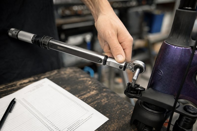 Close-up of a mechanic's hand using a torque wrench on a bicycle component, a paper service checklist visible on the bench